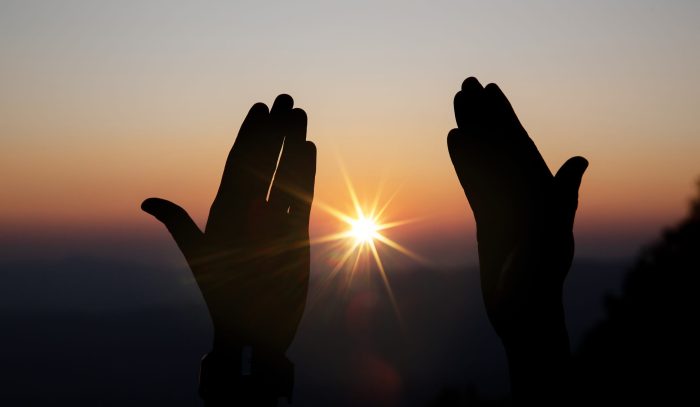Faith of christian concept: Spiritual prayer hands over sun shine with blurred beautiful sunset background